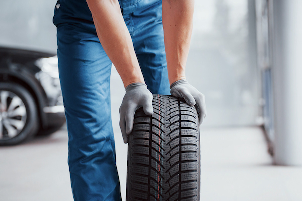 Mechanic with grey gloves rolling car tire