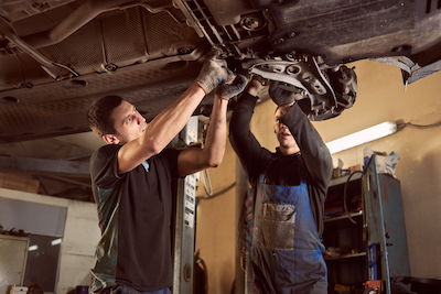 two auto mechanics checking underneath a car transmission